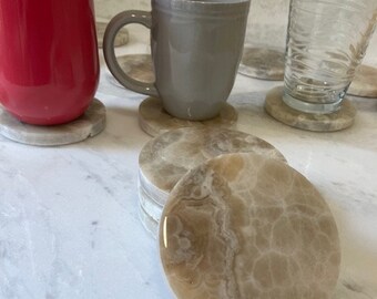 May include: Set of six round beige marble coasters with a white veined pattern. The coasters are stacked on top of each other.