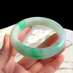 May include: A jade bangle bracelet with a white base and green swirls. The bangle is smooth and polished.