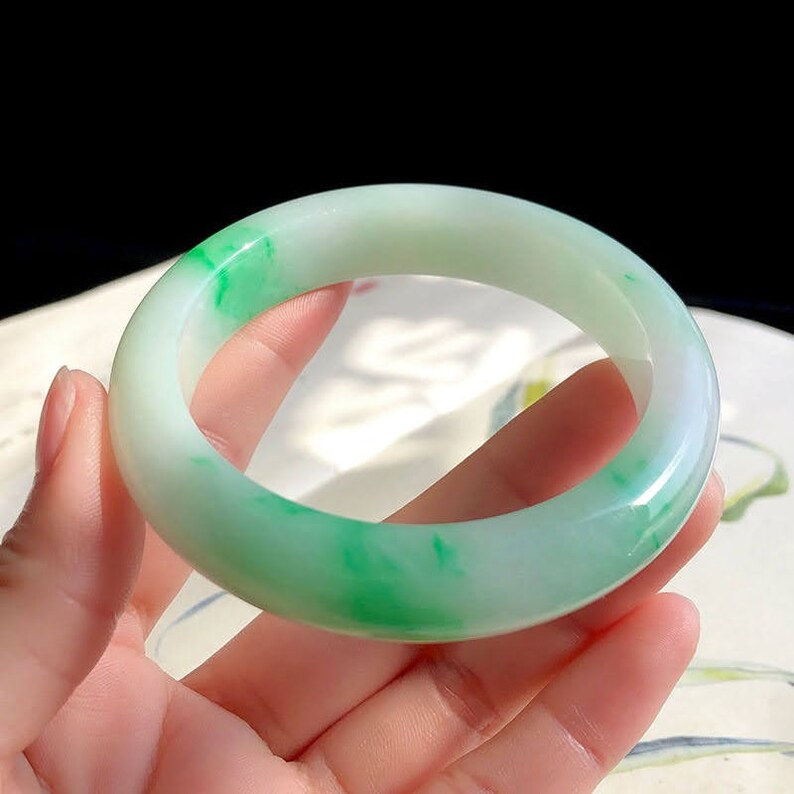 May include: A jade bangle bracelet with a white base and green swirls. The bangle is smooth and polished.