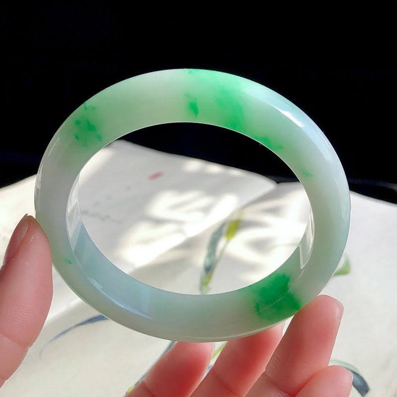 May include: A jade bangle with a white base and green swirls. The bangle is smooth and polished.