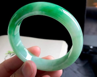 May include: A green jade bangle bracelet with a smooth, polished finish. The bracelet is a light green color with a white undertone.