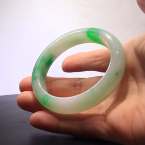 May include: A white jade bangle with green accents. The bangle is smooth and polished.