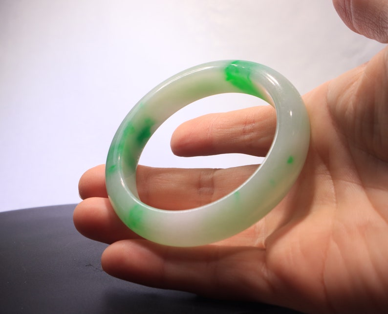 May include: A white jade bangle with green accents. The bangle is smooth and polished.
