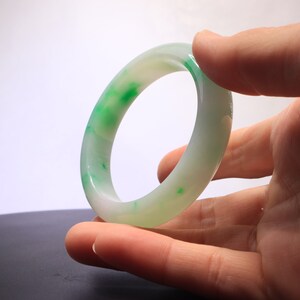 May include: A white jade bangle with green swirls and speckles.