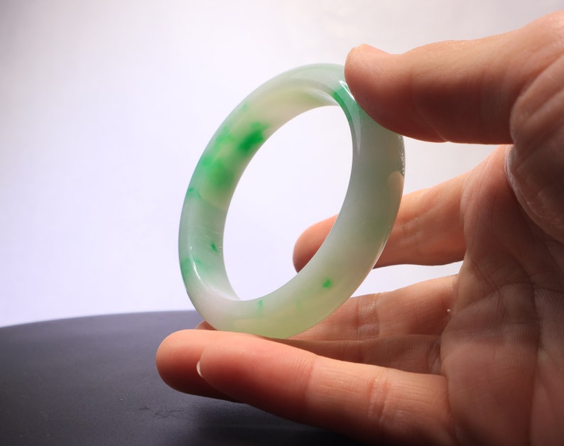 May include: A white jade bangle with green swirls and speckles.