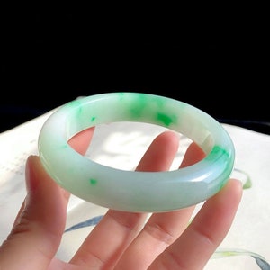 May include: A jade bangle bracelet with a white base and green swirls. The bangle is smooth and polished.