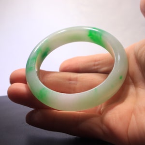 May include: A white jade bangle with green accents. The bangle is smooth and polished.