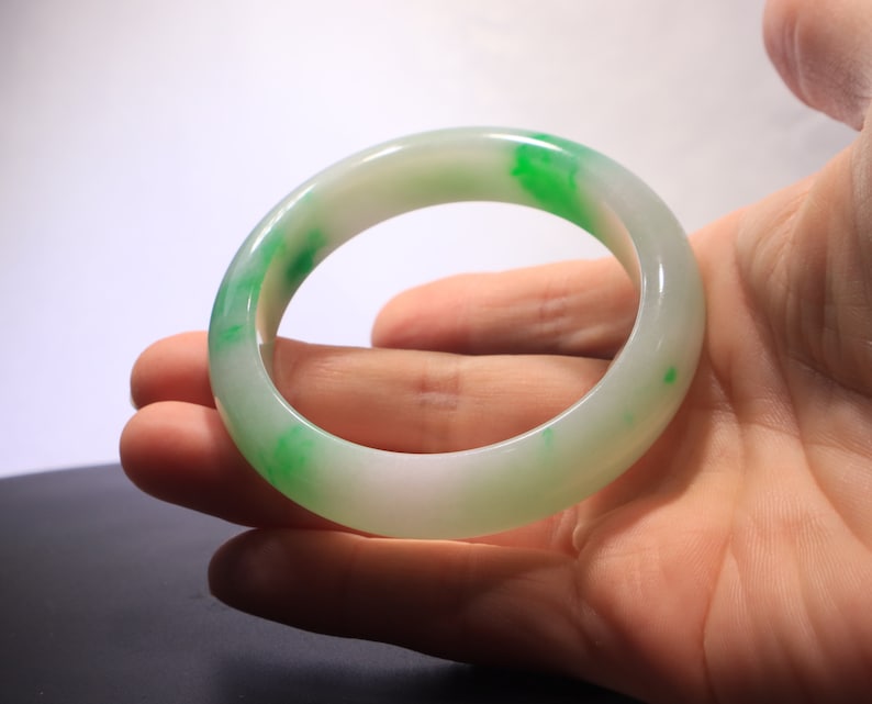 May include: A white jade bangle with green accents. The bangle is smooth and polished.