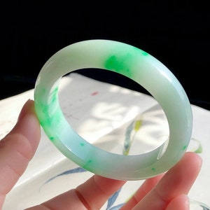 May include: A jade bangle bracelet with a white base and green speckles throughout.