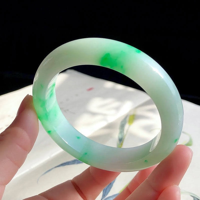 May include: A jade bangle bracelet with a white base and green speckles throughout.