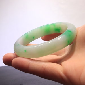 May include: A white jade bangle with green flecks. The bangle is smooth and polished.