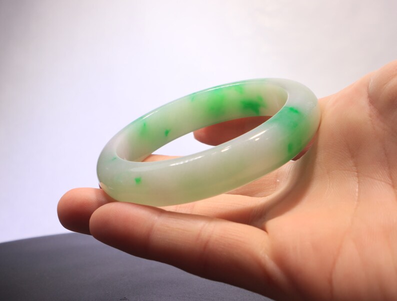 May include: A white jade bangle with green flecks. The bangle is smooth and polished.