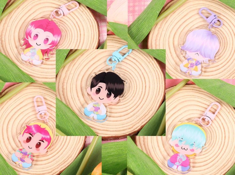 May include: A collection of cartoon character keychains with various hair colors and outfits. Each keychain is attached to a metal clasp. The keychains are arranged on a wooden surface with green leaves.