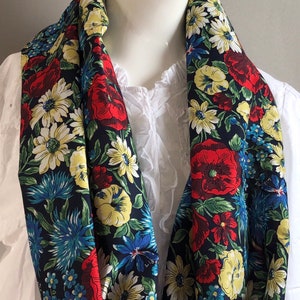 May include: A black floral infinity scarf with red, yellow, blue, and green flowers. The scarf is made of a soft, silky fabric.