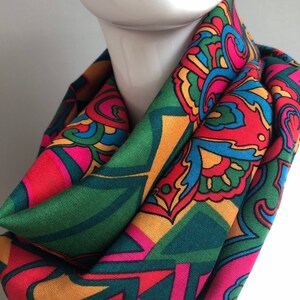 May include: A colorful paisley patterned scarf in shades of green, red, pink, yellow, and blue. The scarf is folded and displayed on a white mannequin.