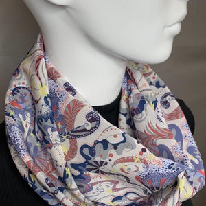 Può includere: Un foulard di seta bianco con un motivo astratto colorato che presenta vortici, punti e forme geometriche in tonalità di blu, rosso, rosa e giallo.