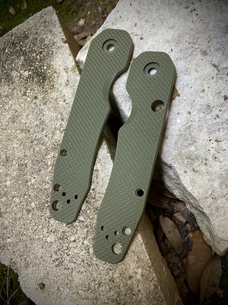 May include: Two green textured knife scales with rounded edges and multiple holes. The scales are made of a durable material and are designed to fit a knife handle.