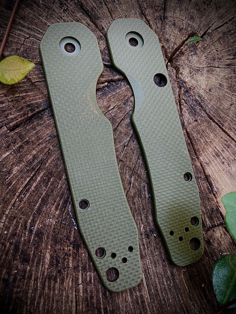 May include: Two green textured knife scales with rounded edges and multiple holes. The scales are made of a durable material and are designed to fit a knife handle.