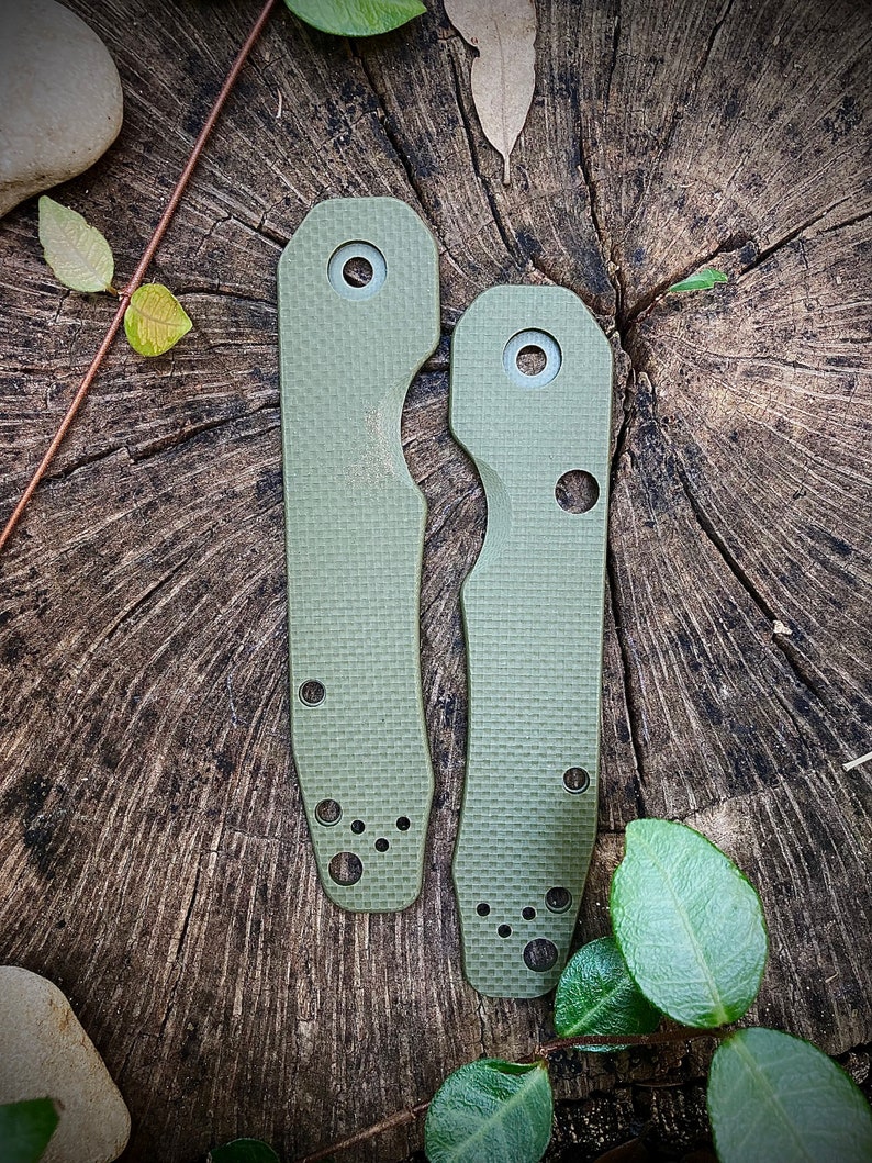 May include: Two green knife scales with a textured surface and multiple holes. The scales are on a wooden surface.