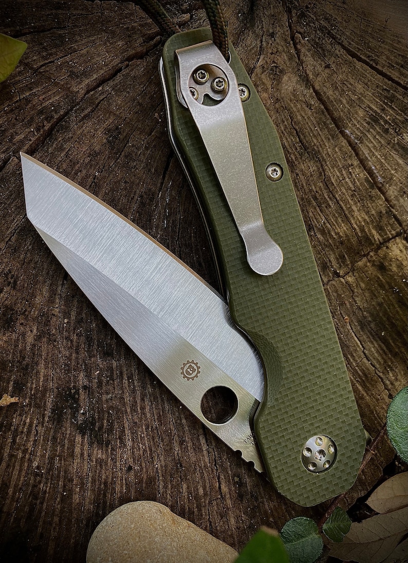 May include: A green folding knife with a silver blade and a pocket clip. The knife has a textured green handle and a silver gear logo on the blade.