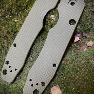 May include: Two green, textured, metal scales for a pocket knife. The scales have multiple holes and a rounded shape.
