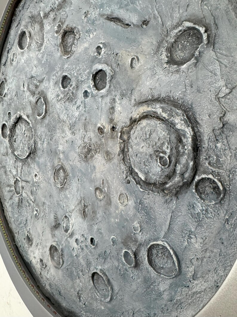 May include: A close-up of a gray and white textured surface with a circular shape. The surface has many craters and indentations, resembling the surface of the moon.
