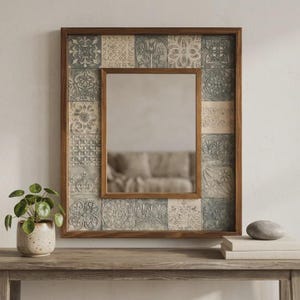 May include: A rectangular wall mirror framed in dark wood, featuring a border of square tiles with embossed floral and geometric patterns in muted shades of grey, blue, and cream. The central glass pane reflects a blurred interior space.