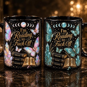 May include: Two black ceramic mugs featuring the text I'm Reading so Fuck Off. The design includes iridescent butterflies, stacked books labelled Dreams, Magic, and Legends, an open book, and crystal clusters in pink and blue colour variations.