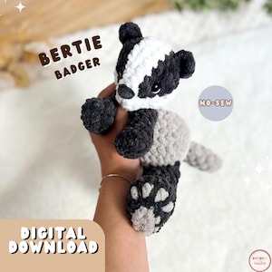 May include: A plush crochet badger toy with black, white, and gray yarn. The badger has a white stripe on its head, black ears, and dark eyes. Text on the image reads: BERTIE BADGER, NO-SEW, and DIGITAL DOWNLOAD. The toy features a soft texture.