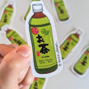 May include: A green and white sticker of a bottle of Japanese green tea. The bottle has a red label with Japanese characters and the text "Oi Ocha" and "Hey There Hot Tea". The sticker also includes the text "16.9 fl oz (1.06 pt) 500 ml".