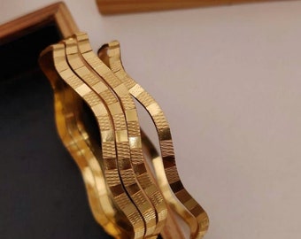 May include: Set of four gold-tone bangles with a wavy, textured design. The bangles are stacked on top of each other in a wooden box.