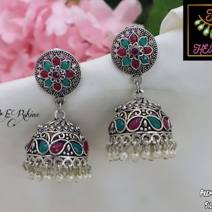 May include: Silver dangle earrings with a floral design and red and green gemstones. The earrings have a bell-shaped bottom with pearl accents.