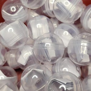 May include: A close-up of a pile of clear plastic balls containing folded pieces of paper. The balls are translucent and show the paper inside.