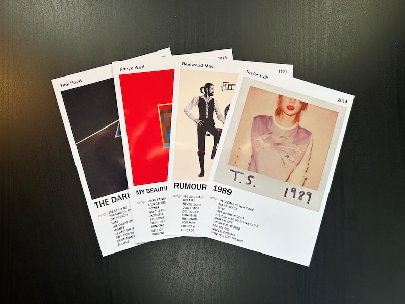 May include: Five album covers, each with a different artist and album title. The covers are arranged in a row, with the top of each cover facing the viewer. The covers are all white with black text and a small image of the album cover art. The album covers are for Pink Floyd's "The Dark Side of the Moon", Kanye West's "My Beautiful Dark Twisted Fantasy", Fleetwood Mac's "Rumours", Taylor Swift's "1989", and Taylor Swift's "1989".
