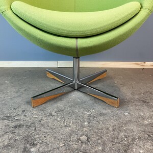 May include: A modern, lime green egg-shaped chair with a stainless steel base and wooden accents. The chair's rounded design features a comfortable, curved seat and backrest. The base has a star-shaped design.