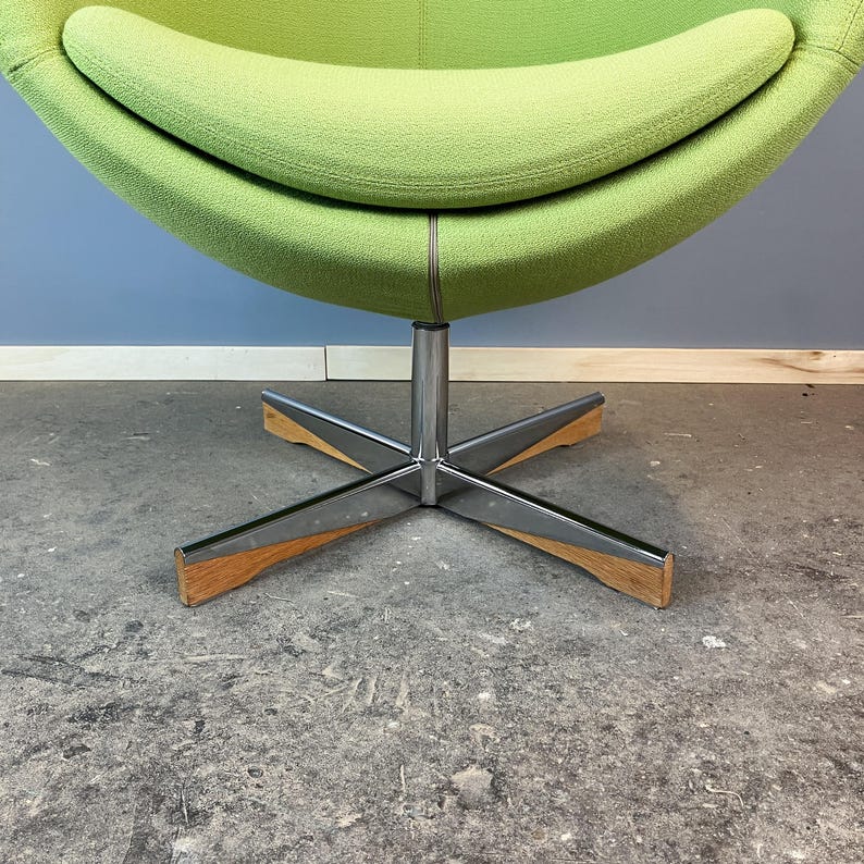 May include: A modern, lime green egg-shaped chair with a stainless steel base and wooden accents. The chair's rounded design features a comfortable, curved seat and backrest. The base has a star-shaped design.