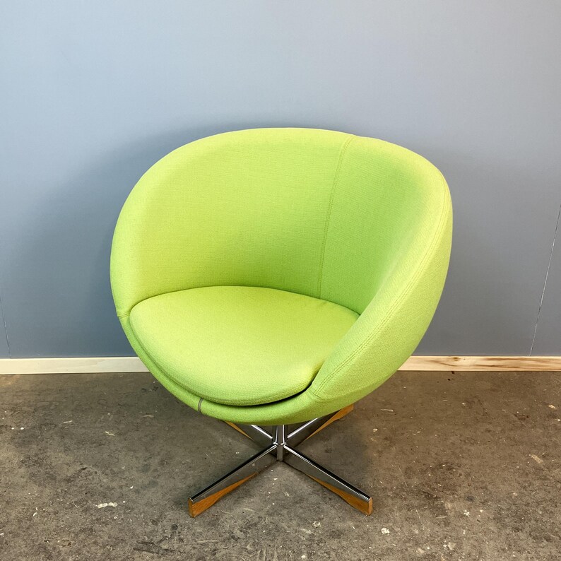 May include: A lime green swivel chair with a rounded back and seat. The chair has a chrome base with wooden accents on the feet. The chair is set against a blue and gray wall.