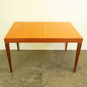 Könnte beinhalten: Ein rechteckiger Holztisch mit einer hellbraunen Tischplatte und vier dunkelbraunen Beinen. Der Tisch ist aus massivem Holz gefertigt und hat ein schlichtes, modernes Design.