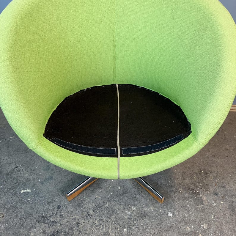 May include: A modern, lime green swivel chair with a black seat cushion. The chair has a rounded back and a chrome base with wooden accents on the feet. The seat cushion is divided into two sections with a white seam.