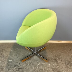 May include: A lime green, mid-century modern style swivel chair. The chair has a rounded, egg-shaped seat and backrest made of textured fabric. It sits on a chrome base with wooden accents. The chair is a vibrant accent piece.