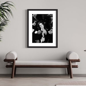 May include: Black and white framed print featuring a woman lighting a cigarette, surrounded by uniformed individuals. The image is a classic, capturing a moment of shared intimacy and defiance. The print is displayed in a modern interior setting.