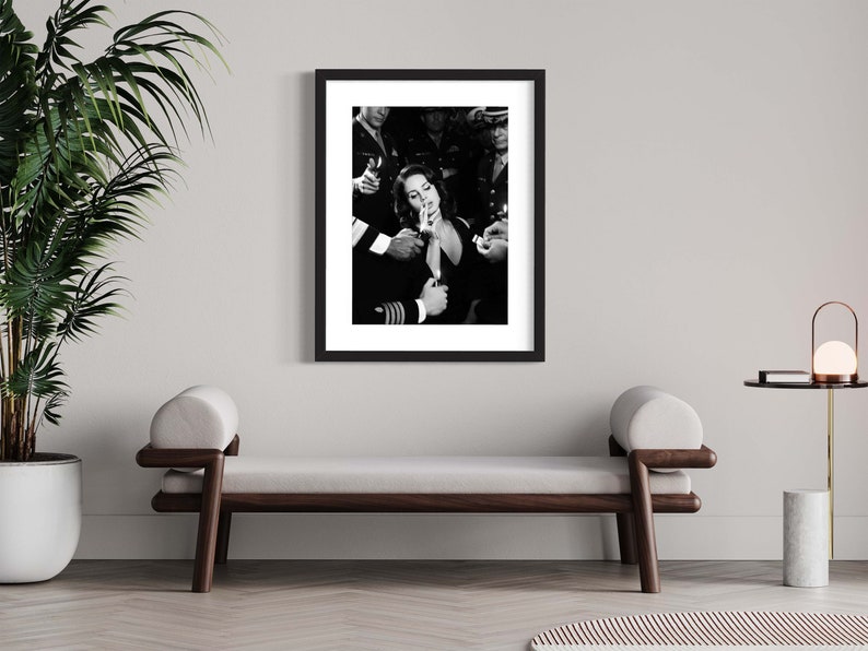 May include: Black and white framed print featuring a woman lighting a cigarette, surrounded by uniformed individuals. The image is a classic, capturing a moment of shared intimacy and defiance. The print is displayed in a modern interior setting.