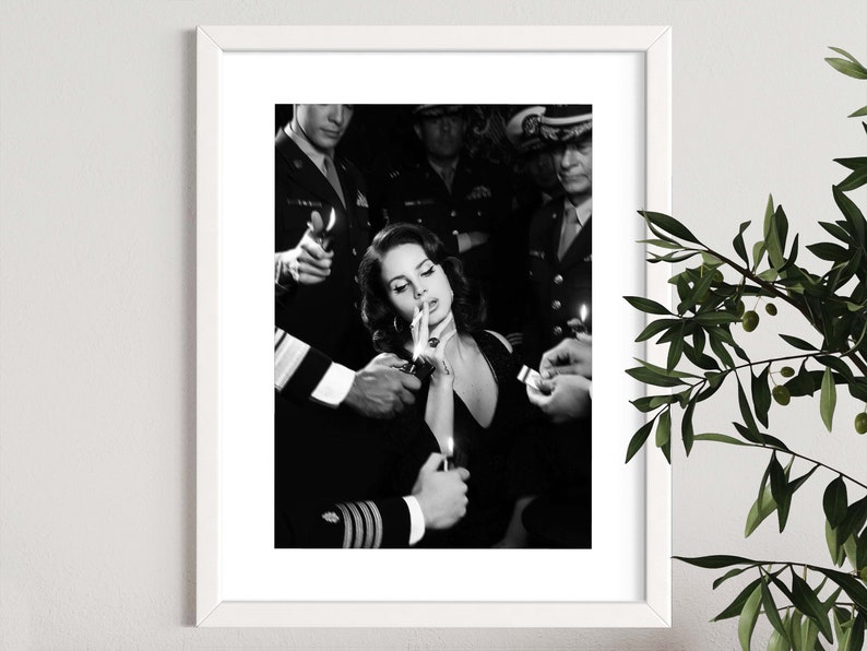 May include: Black and white framed print featuring a woman smoking a cigarette, surrounded by uniformed figures holding lighters. The image has a vintage aesthetic, with a focus on the central figure and the act of smoking.