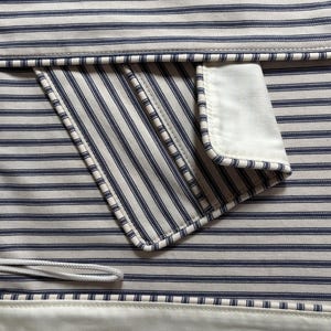 K&ouml;nnte beinhalten: Nahaufnahme eines Stoffes mit blau-wei&szlig;em Streifenmuster. Der Stoff hat eine Tasche mit wei&szlig;em Rand und einem wei&szlig;en Kordelzug. Das Gesamtdesign erinnert an ein klassisches nautisches Thema.