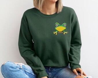 Puede incluir: Una sudadera verde oscuro con un gráfico de rana de dibujos animados en la parte delantera. La rana es verde con ojos amarillos y una boca amarilla.