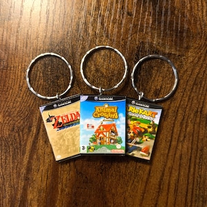 Pode incluir: Três chaveiros prateados com pingentes de cartuchos de jogo. Os pingentes são para os jogos Nintendo GameCube: The Legend of Zelda: The Wind Waker, Animal Crossing e Mario Kart: Double Dash!!