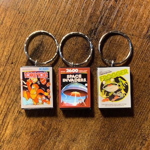May include: Three silver keychains with miniature Atari video game cartridges attached. The cartridges are for the games Donkey Kong, Space Invaders, and Frogger.