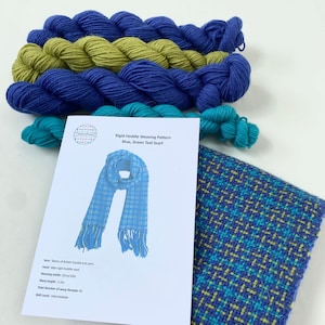 May include: A rigid heddle weaving pattern for a blue, green and teal scarf. The pattern includes instructions for a scarf with a chequered design. The yarn is shown in skeins and the finished scarf is shown in the image.