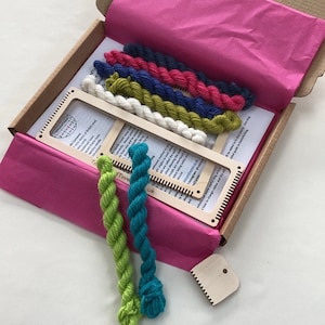 May include: A wooden loom kit with colorful yarn in a cardboard box. The kit includes a wooden loom, yarn in various colors, a comb, and instructions. The yarn is arranged in a rainbow pattern.