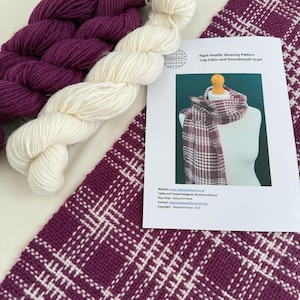 May include: A close-up of weaving supplies, including skeins of white and deep purple yarn, a woven scarf with a plaid pattern, and a pattern sheet. The scarf and pattern sheet feature a Log Cabin and Houndstooth design.